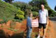 Elderly woman and man standing next to a hole holding a red and white sign