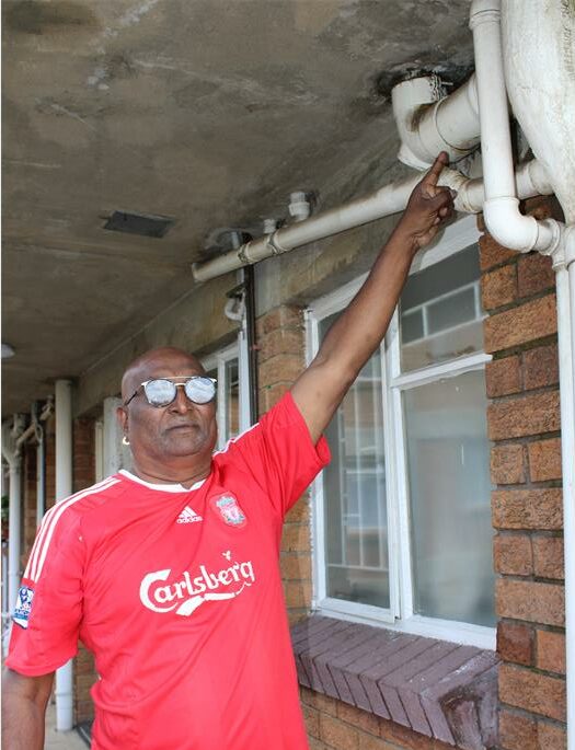 Indian man with red shirt pointing to a pipe