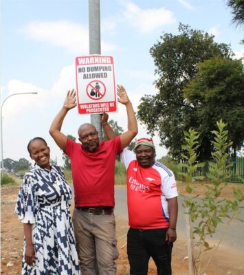 Three black people, one woman and two men stranding at a street pole