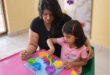 Indian woman sits next to an Indian girl at a pink table