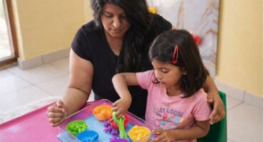Indian woman sits next to an Indian girl at a pink table