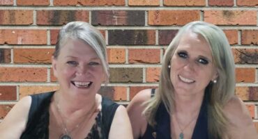 Two women sitting in front of a brick wall