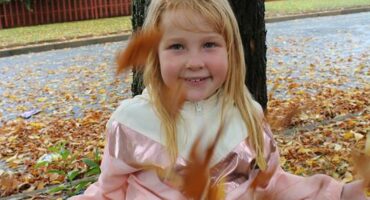Red haired girl sitting in in front of a tree with autumn leaves spiralling around her