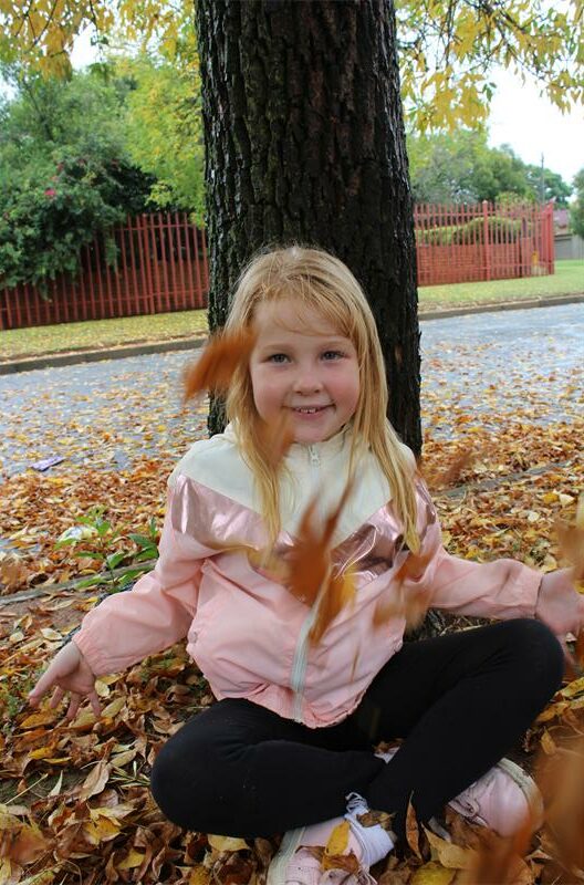 Red haired girl sitting in in front of a tree with autumn leaves spiralling around her