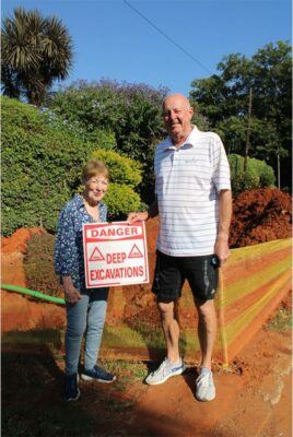 Woman and man holding a red and white deep excavation cautionary board