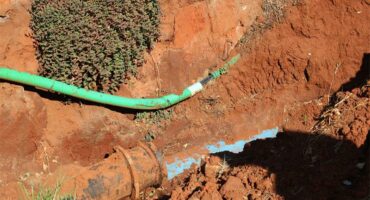 Deep excavation with a green pipe sagging onto a blue water pipe