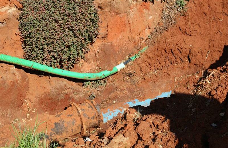 Deep excavation with a green pipe sagging onto a blue water pipe