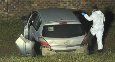 Man in white overall standing next to a car