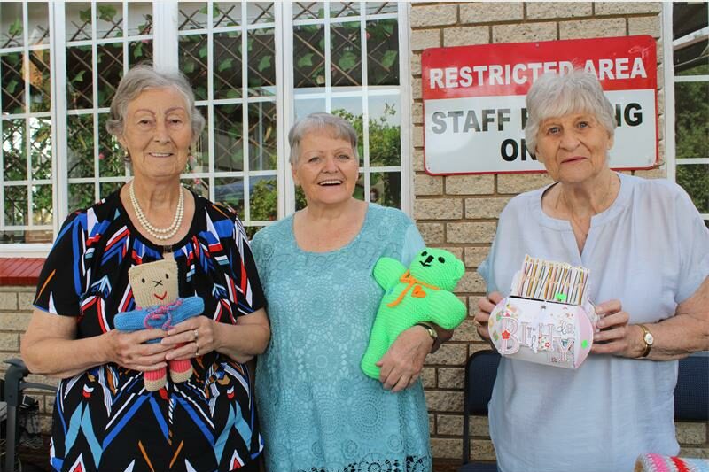 Three elderly women holding home-made items