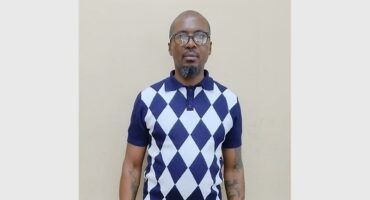 A man standing, wearing spectacles.