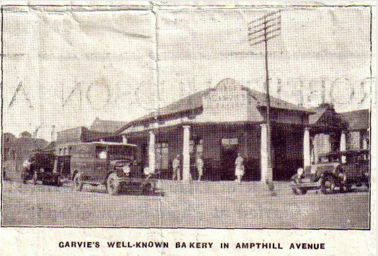 A black and white photo of an old building with two old cars parked outside.