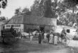 A black and white photo of an old bakery building, horse-drawn cart and people standing in front of the building.