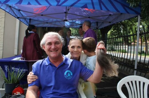 Grey haired man holds a ponytail of hair while a woman holding a child looks over his shoulder.