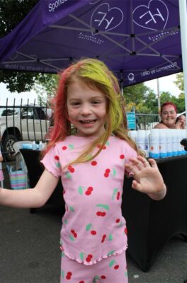 Little girl wearing a pink outfit waves and smiles.