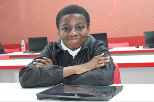 A young boy smilling at the camera with his arms folded.
