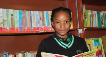 A little girl holding a book,smilling at the camera.