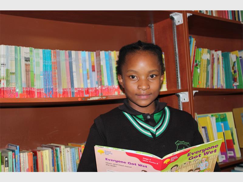 A little girl holding a book,smilling at the camera.