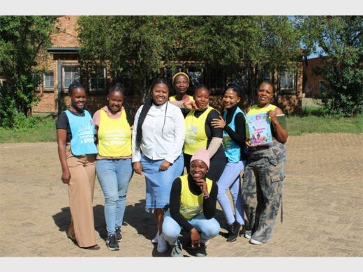 7 ladies standing with one guy wearing colourful bibs.