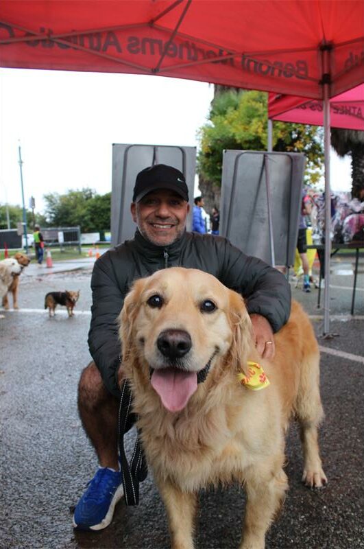 Man with a black cap holding a dog with its tongue sticking out