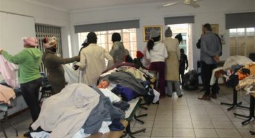 Tables with secondhand clothing on them in a clubhouse with people looking for bargains.