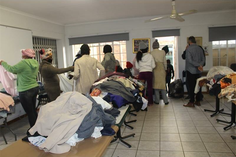 Tables with secondhand clothing on them in a clubhouse with people looking for bargains.