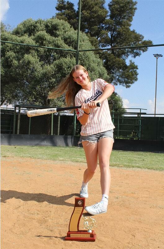 Girl swinging a baseball bat with a trophy in the foreground