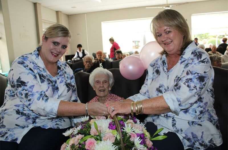 Twee vrouens hou blomme ruiker voor bejaarded dame