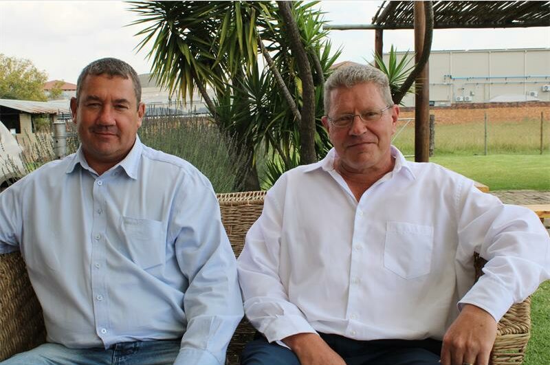Two white men sitting on a couch in a garden setting
