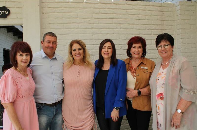 Image of five women and a white man standing against a white wall