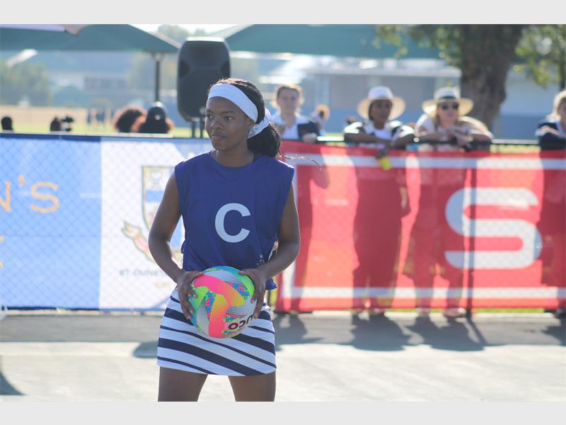 A netball player on court in blue and white kit with a white headband and a C on her shirt.