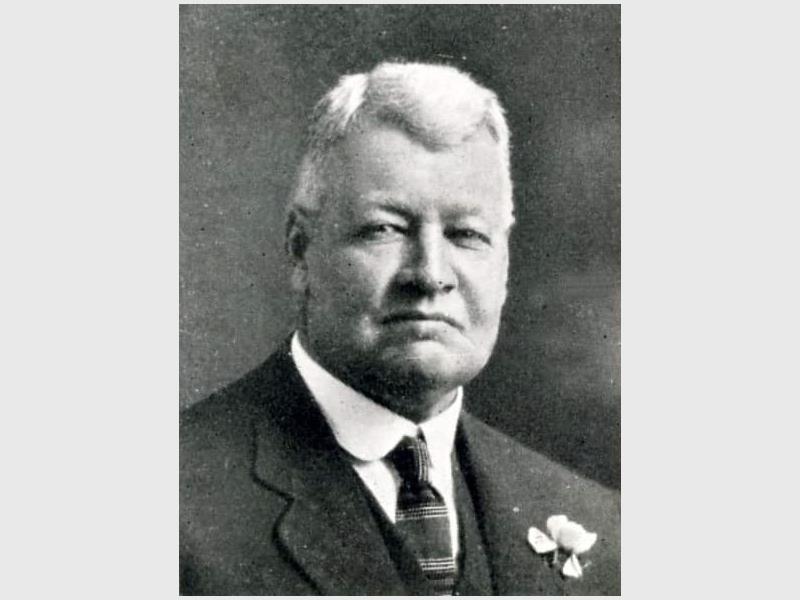 A black and white image of a white male with grey hair and wearing a suit and tie.