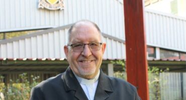 Elderly man holding a glass trophy standing in front of a building with a school emblem