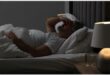 A man lying in bed with his hand on his forehead.