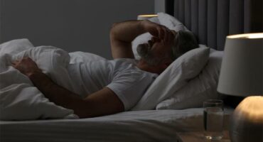 A man lying in bed with his hand on his forehead.