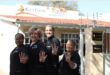 Four women wearing black show their hands with four fingers up in front of a business