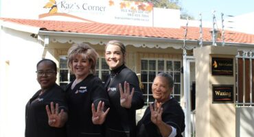 Four women wearing black show their hands with four fingers up in front of a business