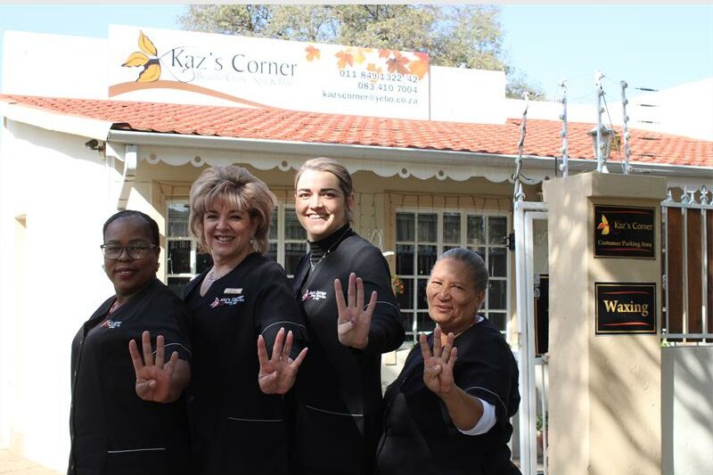 Four women wearing black show their hands with four fingers up in front of a business