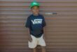 Black boy wearing a green cap standing in front of a garage door