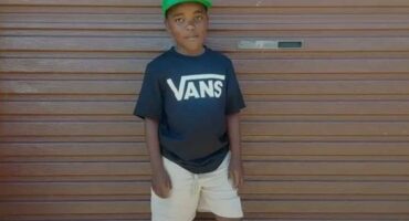 Black boy wearing a green cap standing in front of a garage door