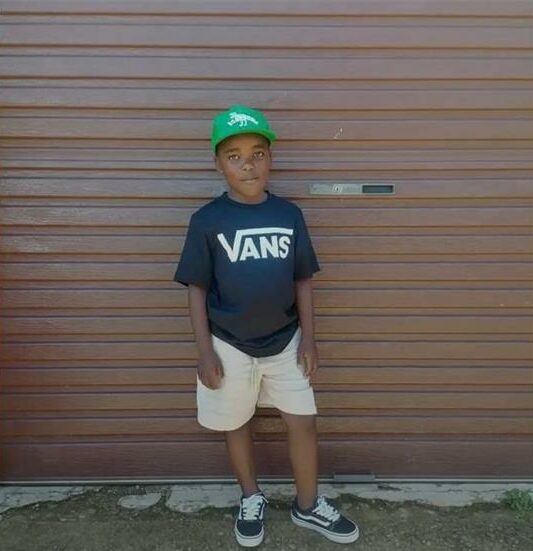 Black boy wearing a green cap standing in front of a garage door