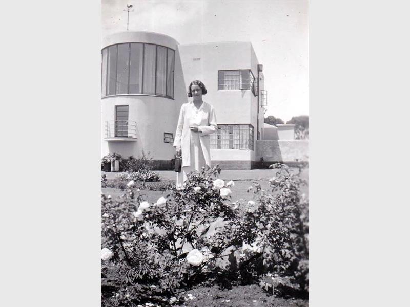 A woman standing in a garden with an art deco house in the background, in the 1930s.