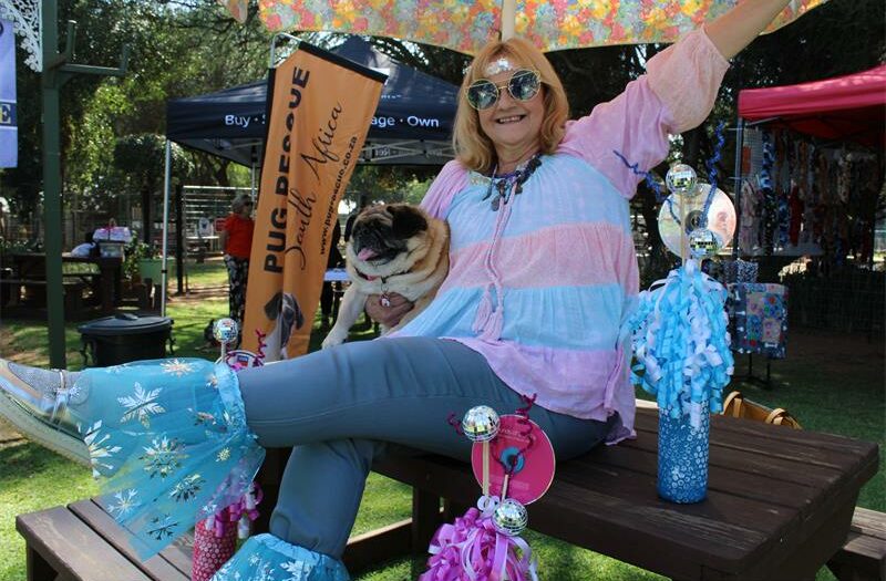 Woman wearing disco costume sits on a table, holding a pug