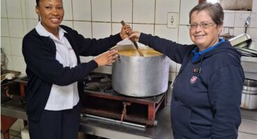 Two women, one black and one white stirring a pot of soup