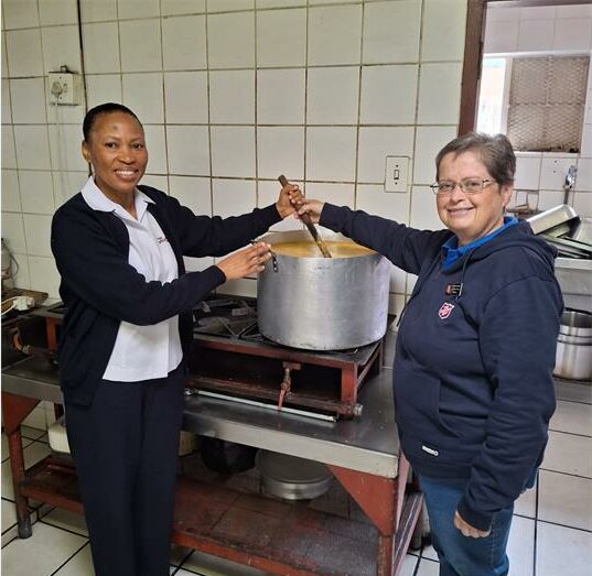 Two women, one black and one white stirring a pot of soup