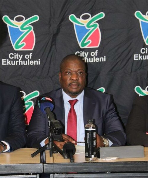 Executive Mayor Nkosindiphile Xhakaza sitting at a desk with the Ekurhuleni Metro back drop