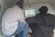 Tow men have their backs to the camera as they sit in a police van