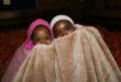 Two coloured girls are wrapped in a blanket with their faces covered