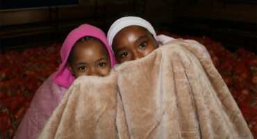 Two coloured girls are wrapped in a blanket with their faces covered