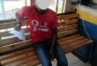 Man wearing a red shit shits on a bench. His face is blocked out