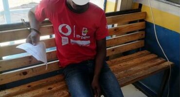 Man wearing a red shit shits on a bench. His face is blocked out